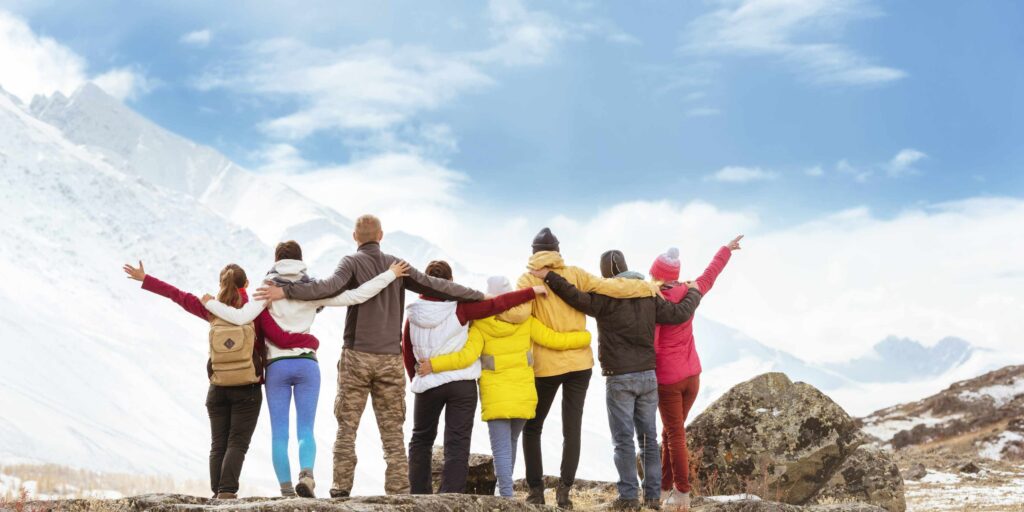 Big group of happy friends standing hugging and looking at mountains travel incentive