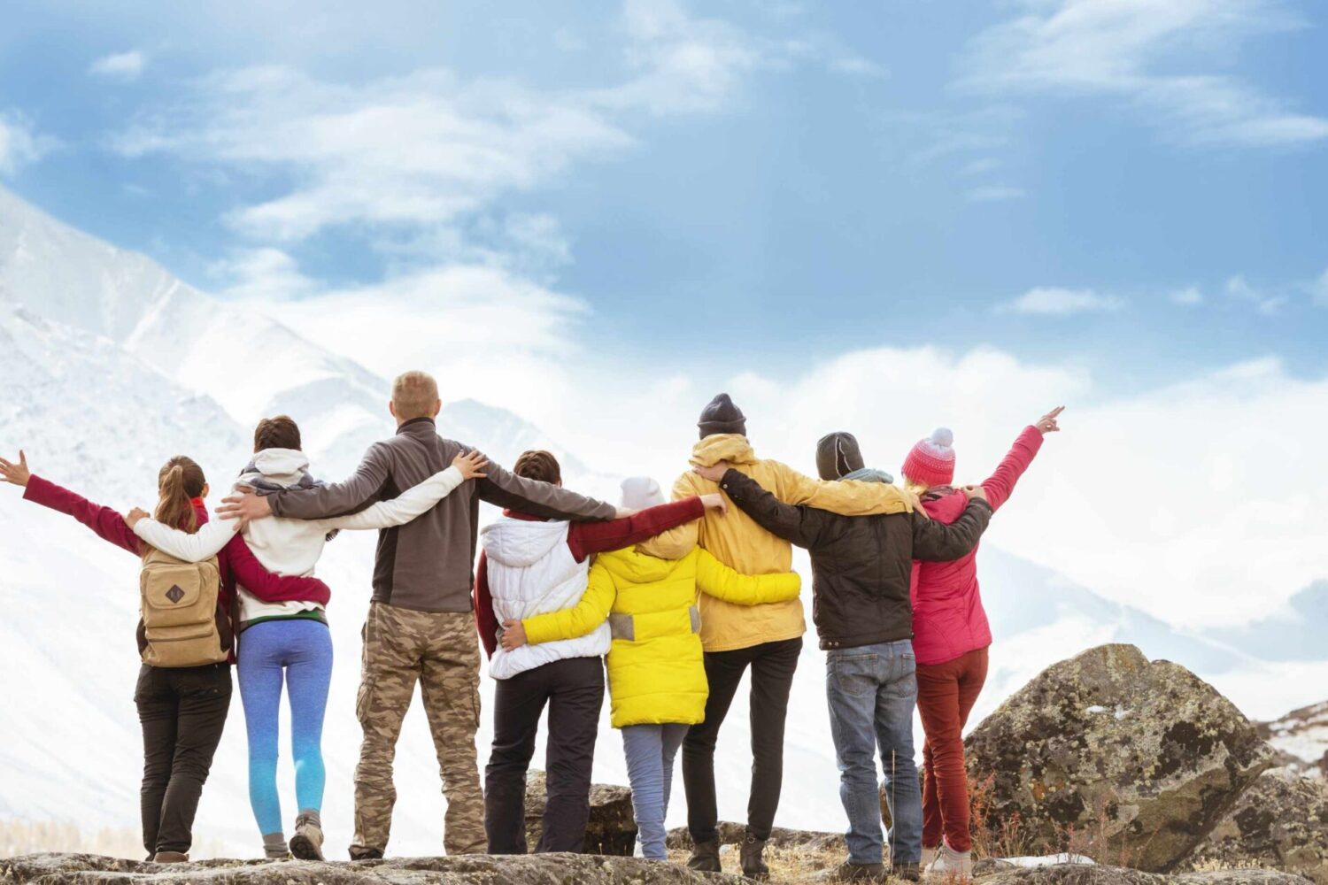 Big group of happy friends standing hugging and looking at mountains travel incentive